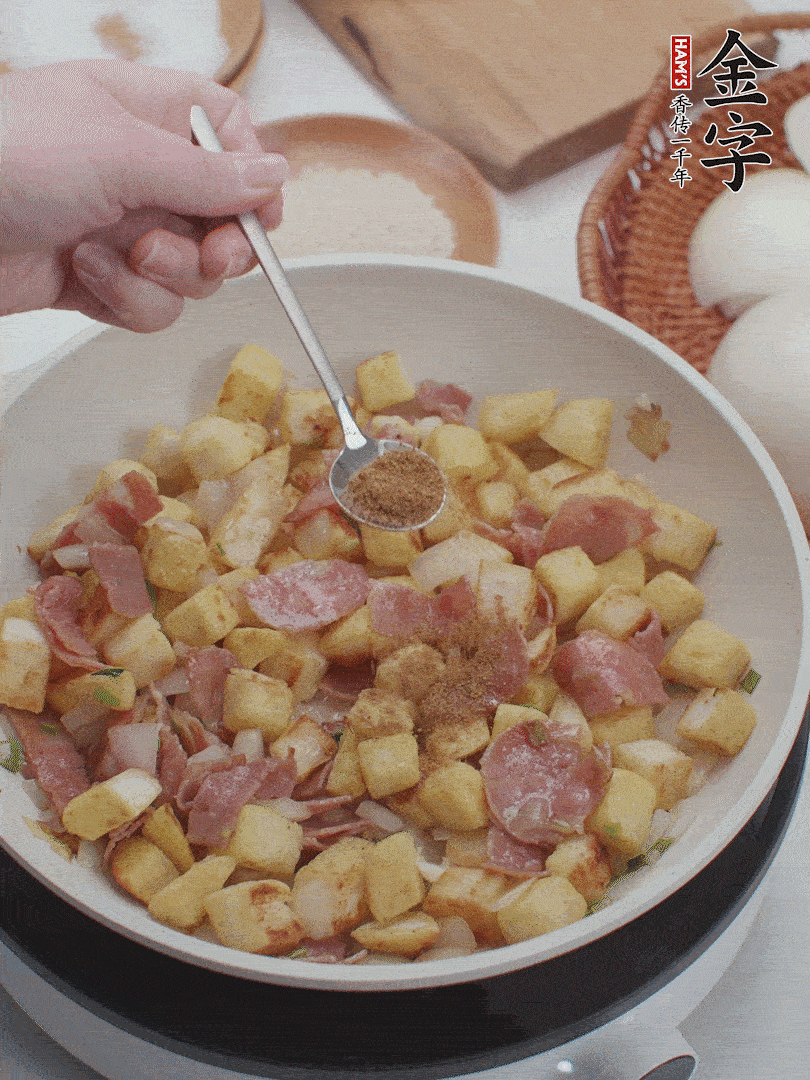 起鍋少油，煸香洋蔥丁、蔥白，加入金字培根火腿翻炒幾下，再加入饅頭丁、1小勺孜然粉、少許鹽翻炒均勻并鋪平。